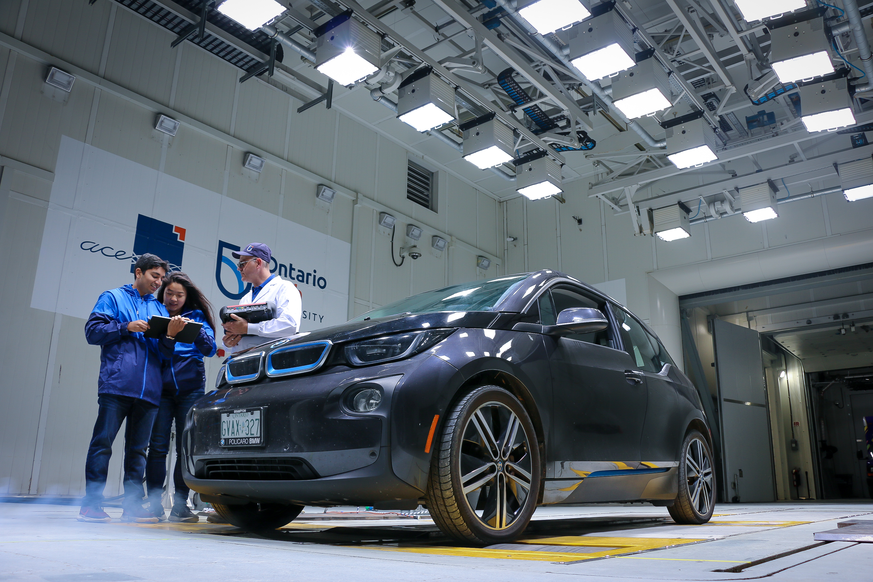 Two ACE students with an ACE engineer examining a car in the climatic wind tunnel.