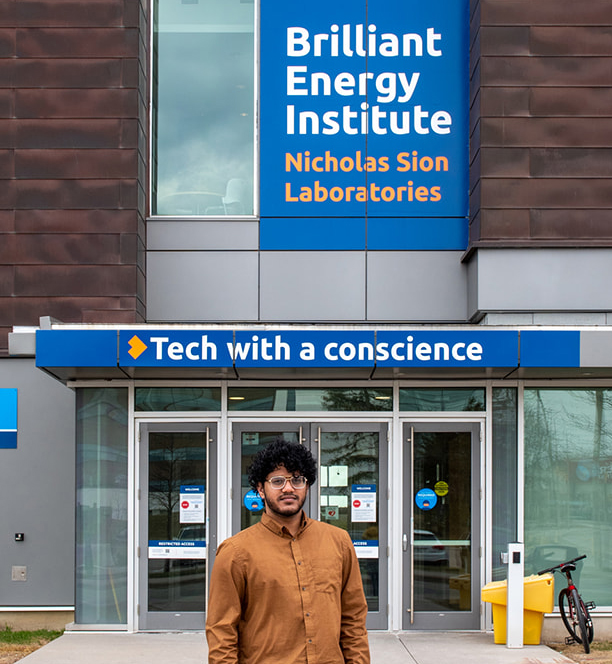 Ammar Zia, Biological Science, class of 2022, standing in front of the Nicholas Sion Laboratories banner at the exterior of the Energy Systems and Nuclear Science Research Centre.
