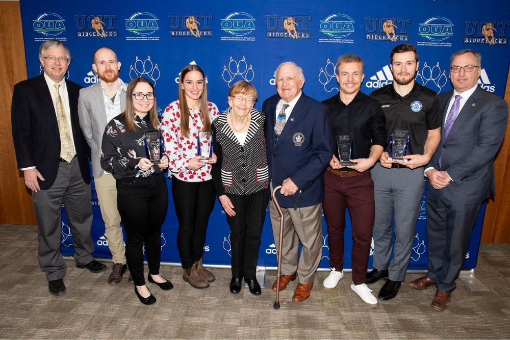 Bob and Sally Baun and student award recipients stand behind an Ontario Tech backdrop smiling at the camera.