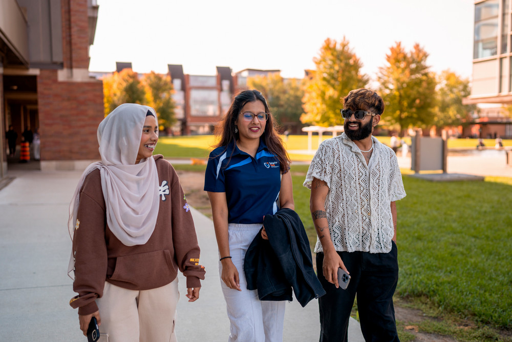 Three Ontario Tech students walk outside on the edge of Polonsky Commons on a fall day. 