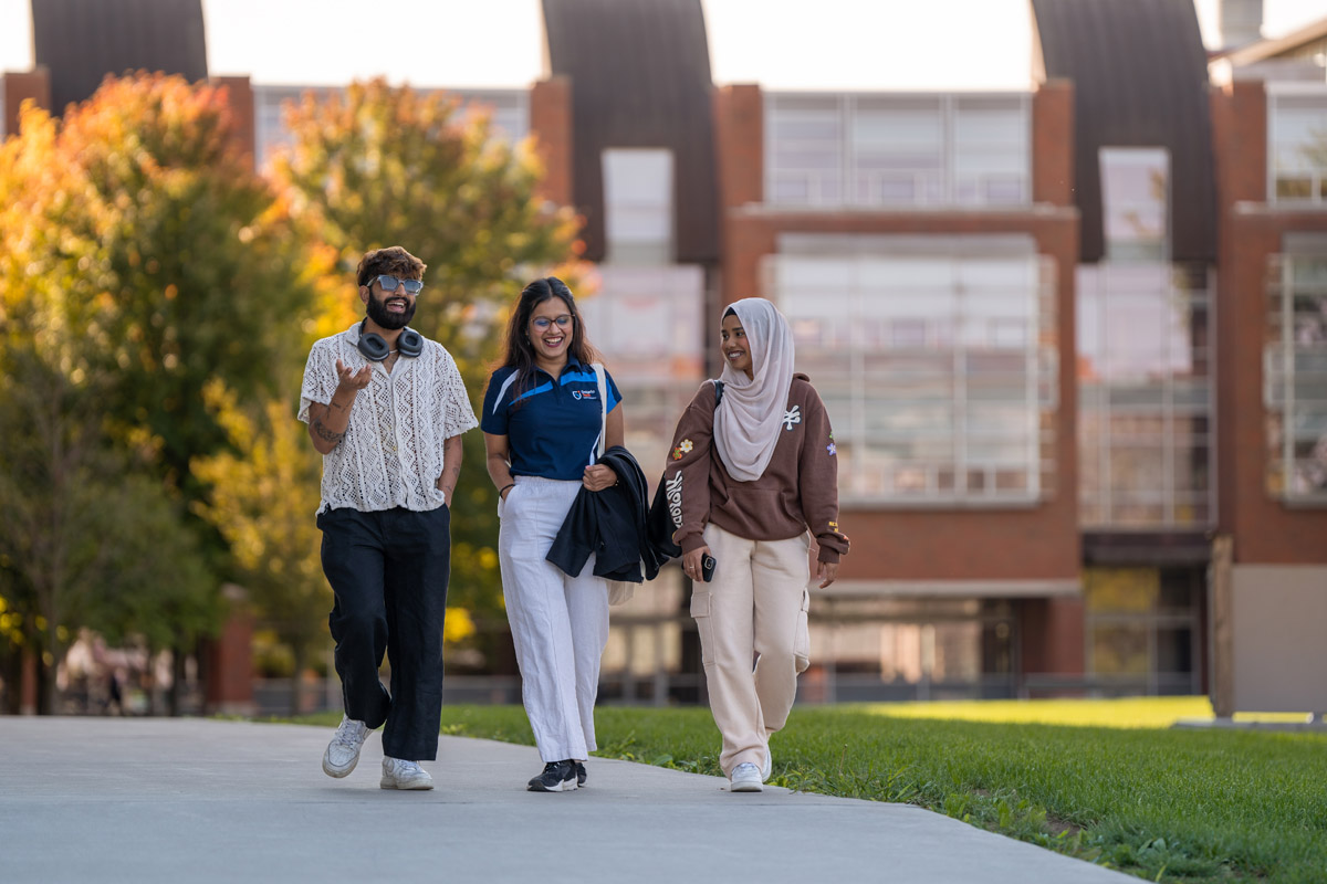 Three students walk together outside on campus, smiling and talking to each other.