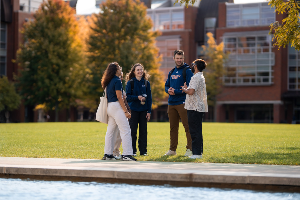 Four students stand beside the reflecting pond on Polonsky Commons, laughing and smiling with each other.