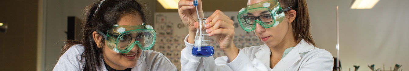 Two students in a science lab using an eye dropper and beaker.