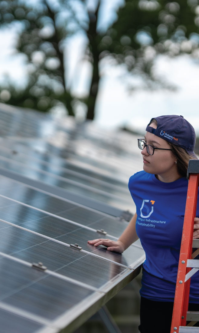An Ontario Tech student stands on a ladder inspecting a solar panel.