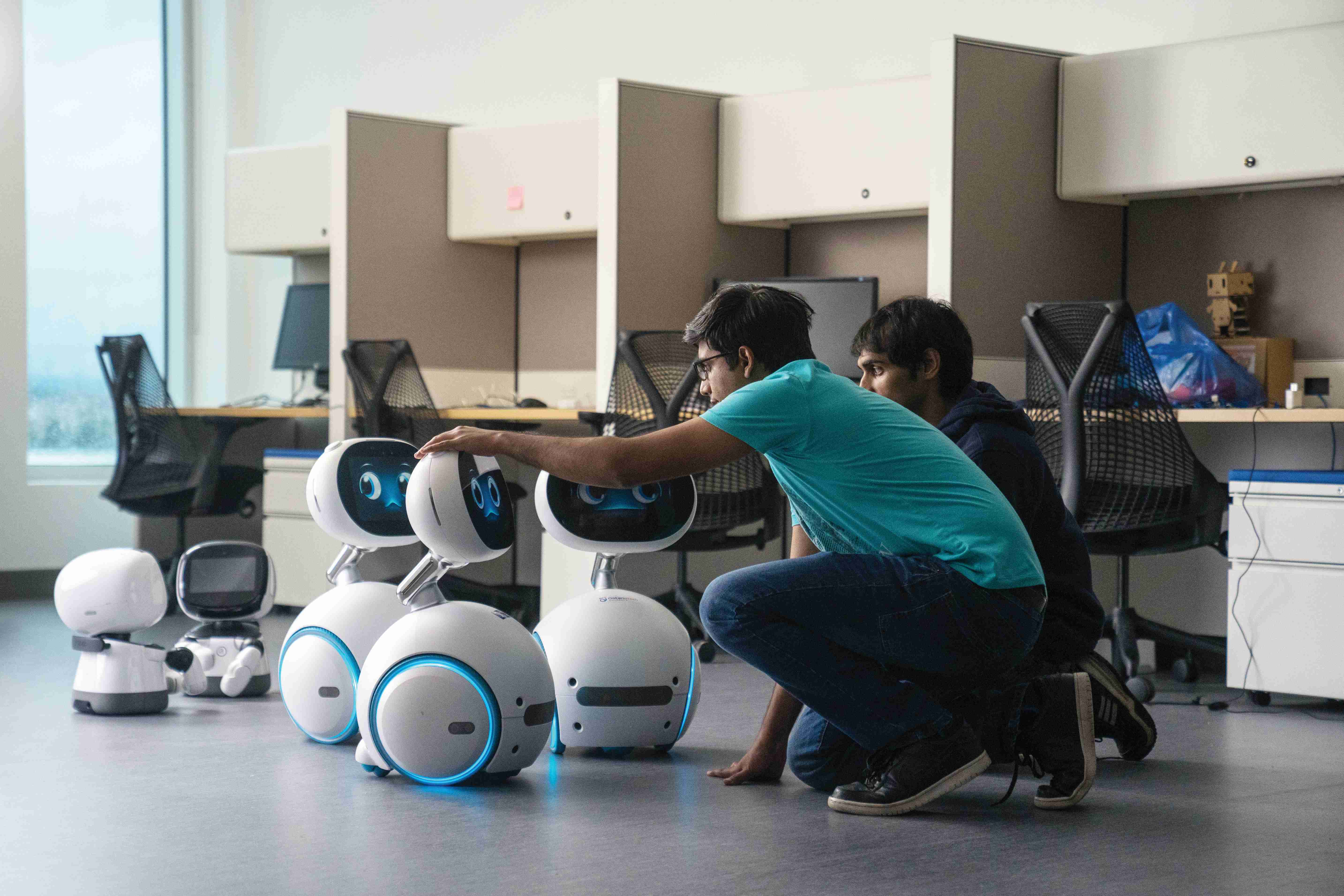Two students kneel down with robots around them.