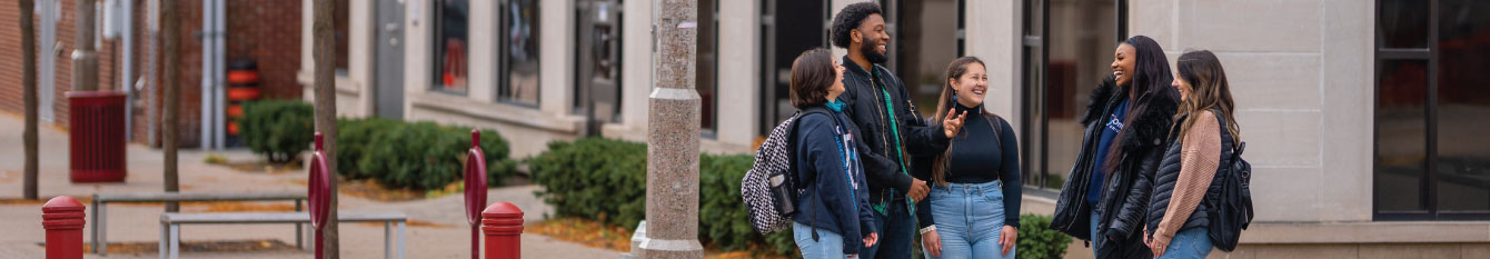 A group of students stand talking and smiling outside of Bordessa Hall at the downtown Oshawa campus location.