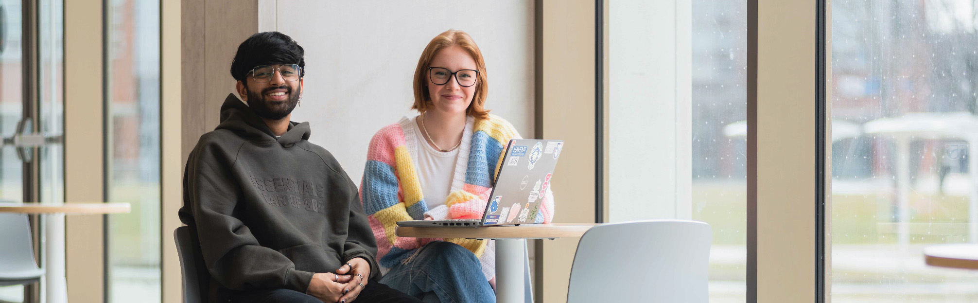 Two students sitting at a small round table in Shawenjigewining Hall with a laptop in front of them. 