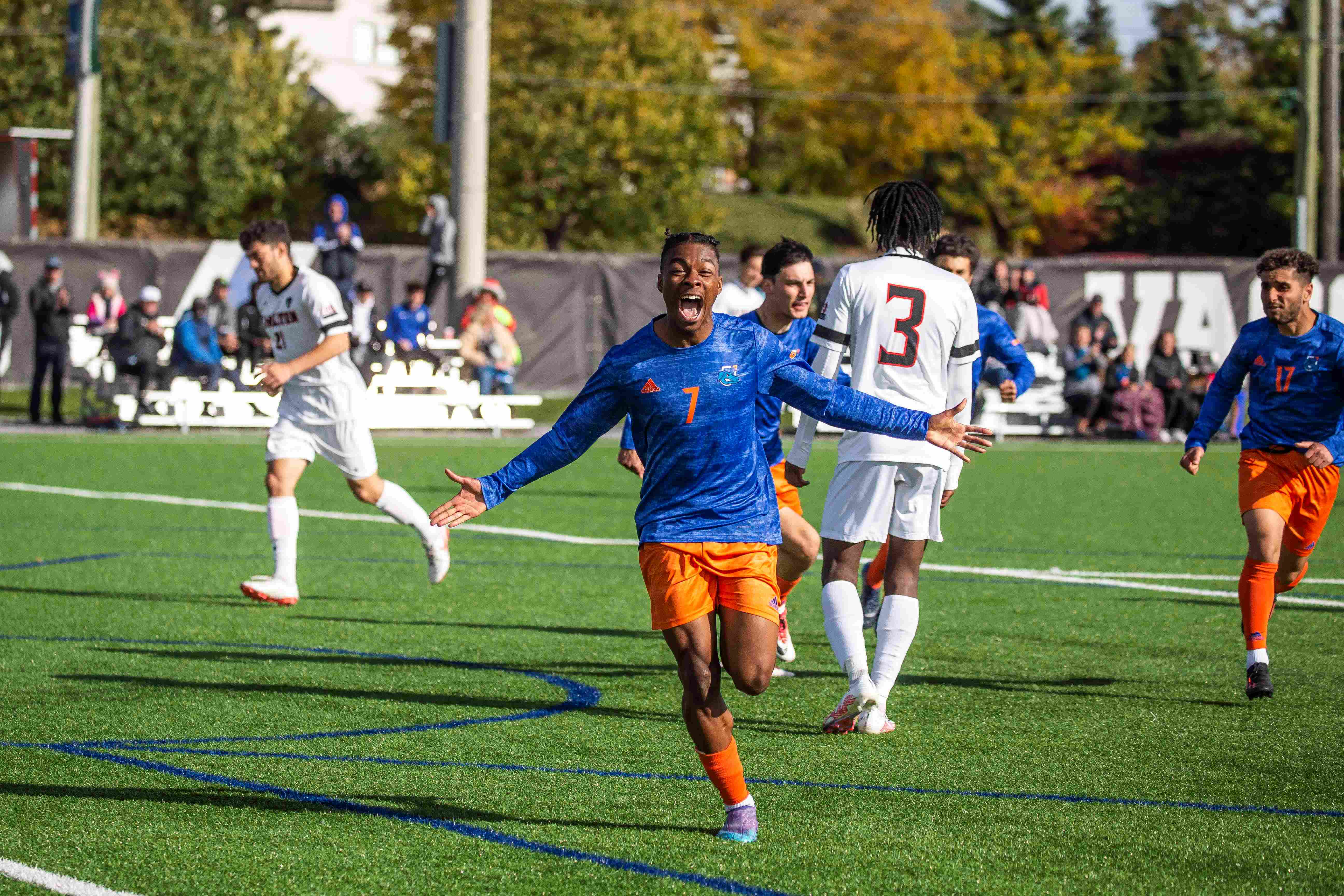 A member of the men's soccer team celebrates with his arms wide open after scoring a goal.