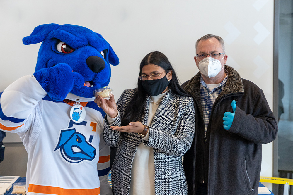 Hunter the Ridgeback mascot standing with a student and President Steven Murphy, celebrating Pi Day