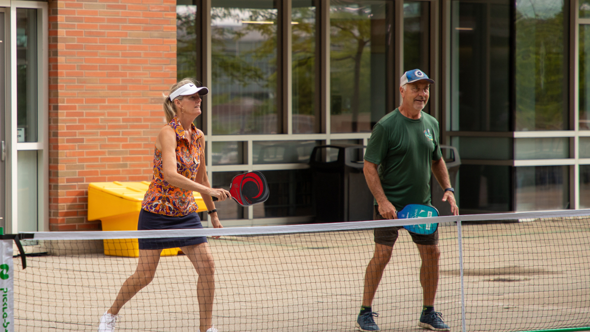 a woman and a man are on the other side of a net with pickle ball paddles