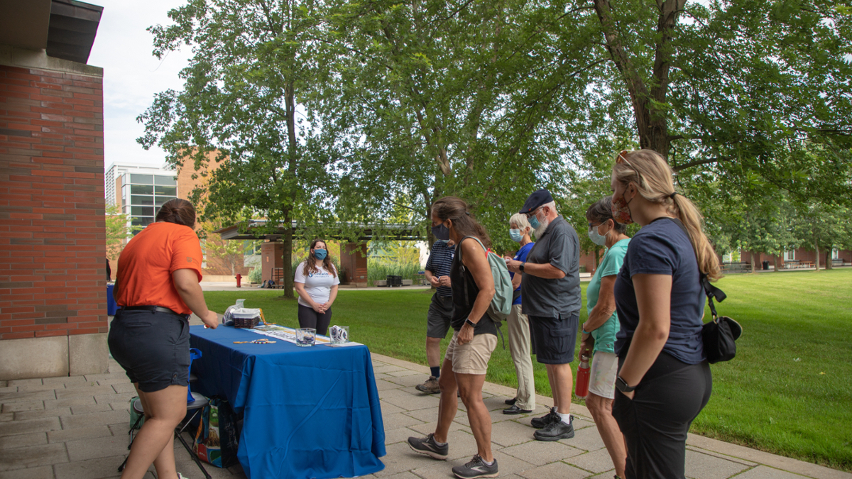 Students and older adults standing around a table outside on polonsky commons on a summer day