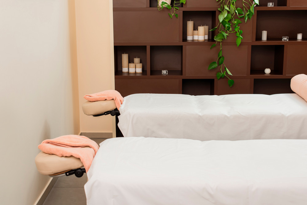 stock photo of massage tables with towels set up at the head. a brown shelving unit is in the background with candles 