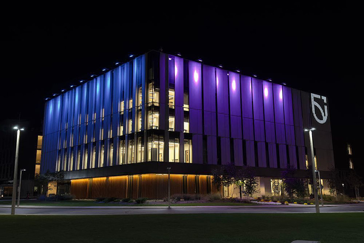 Shawenjigewining and Bordessa building at night illuminated with vertical bands of purple and blue lights