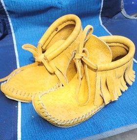 A pair of yellow suede moccasin-style shoes with fringes.