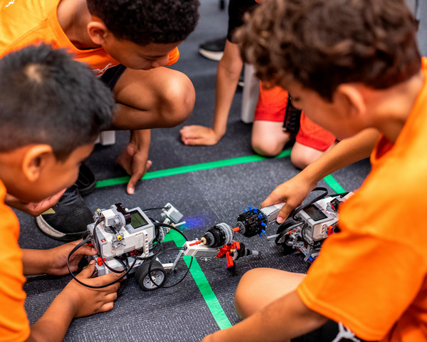 Kids build robotics on a carpet.