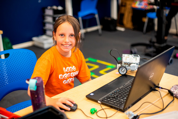 A camper in an orange t-shirt using a laptop at the 2023 Summer Camps.