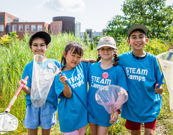 Four campers outside holding bug nets at the pond on the Ontario Tech campus.