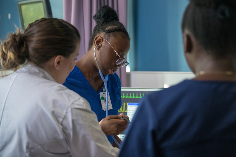 three nursing students next to each other looking at a nursing mannequin  facing 