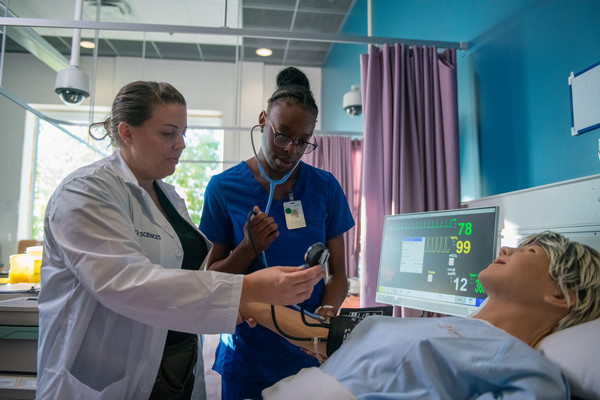 image of a nursing student and instructor standing over a nursing mannequin in bed