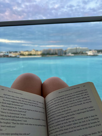 Open book resting on an individuals knee with a city in the background 