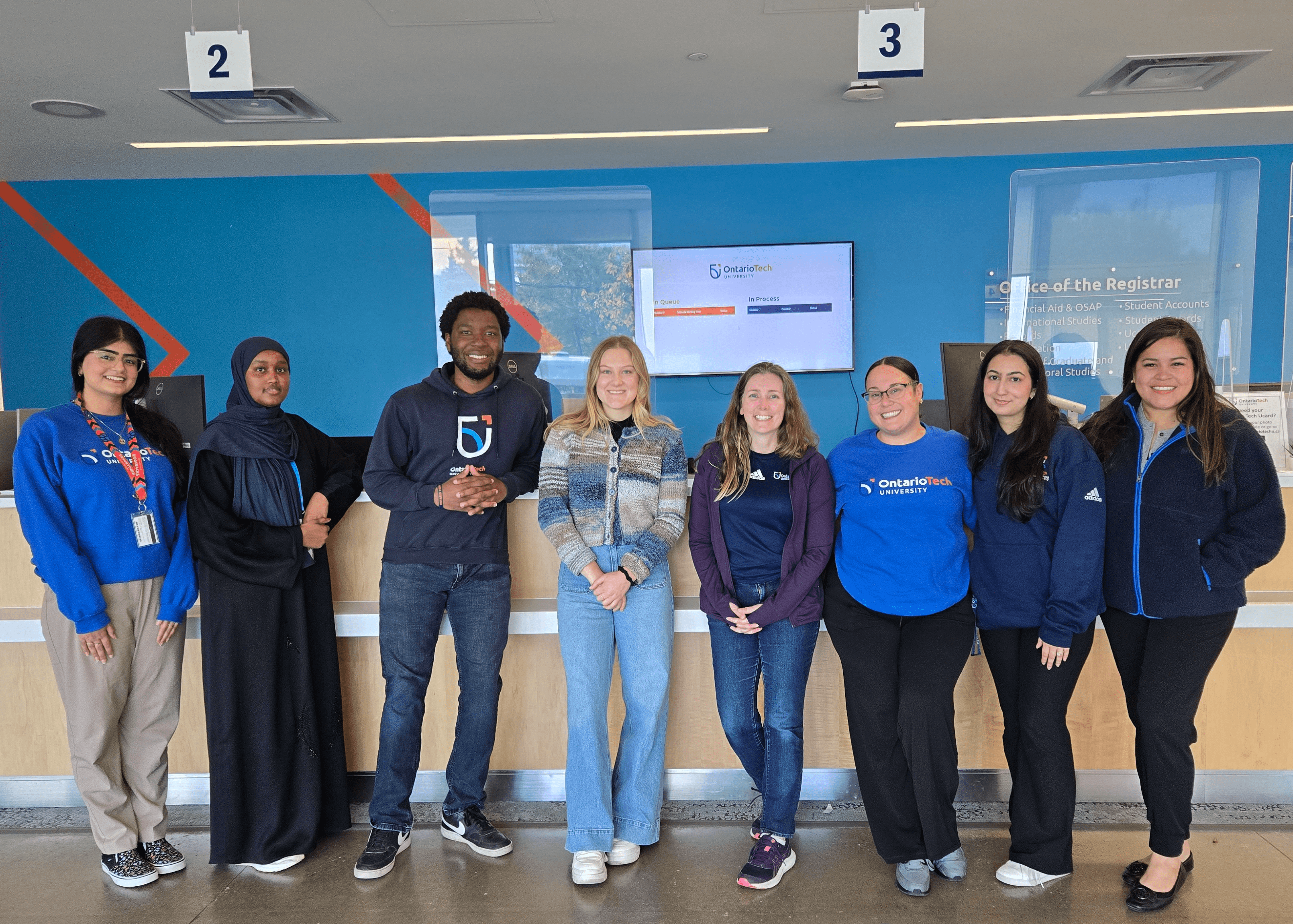 Ontario Tech University staff smiling inside the Office of the Registrar, wearing blue clothing.