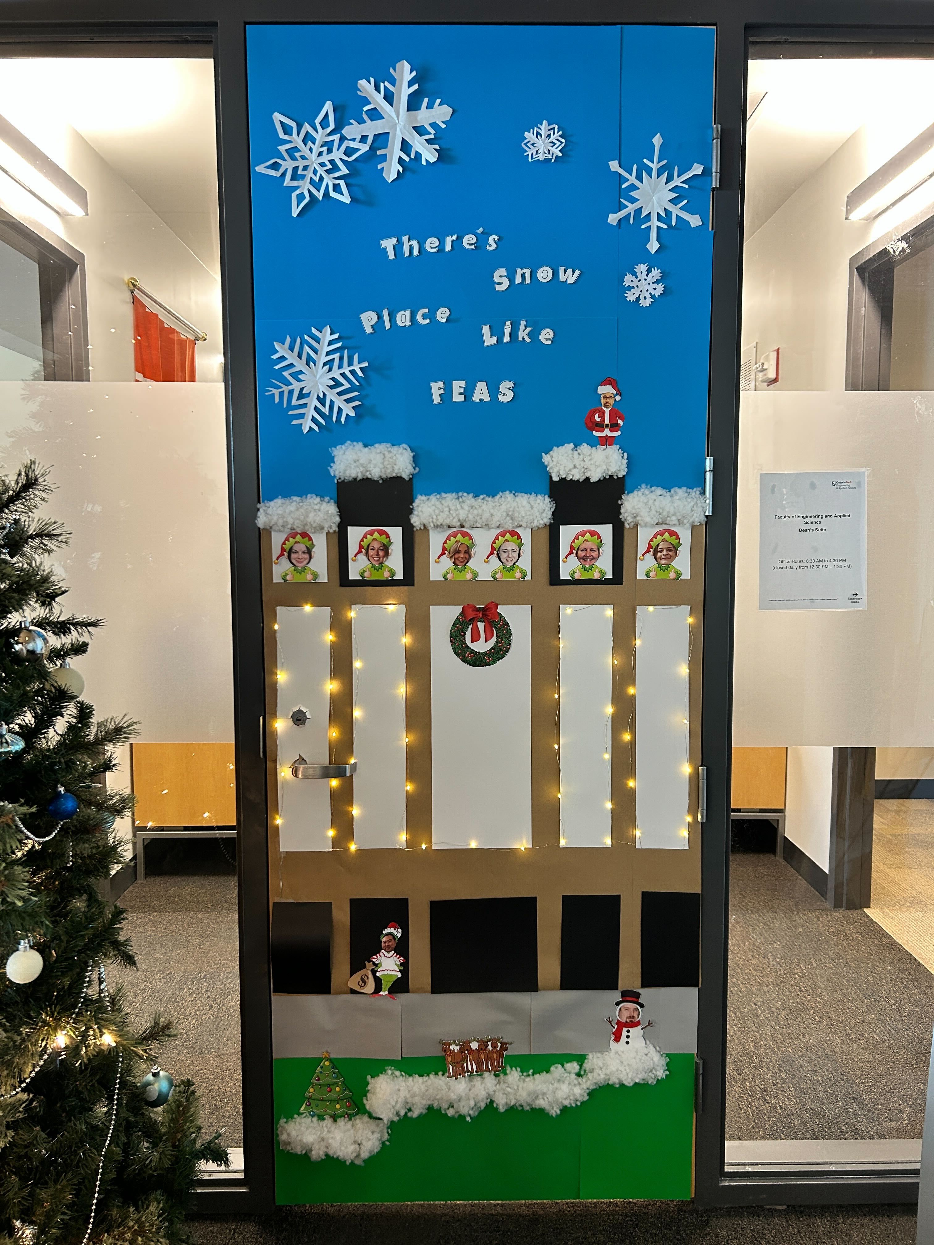 A festive holiday door decoration featuring snowflakes, lights, and characters, with the phrase "There's snow place like FEAS" displayed prominently.