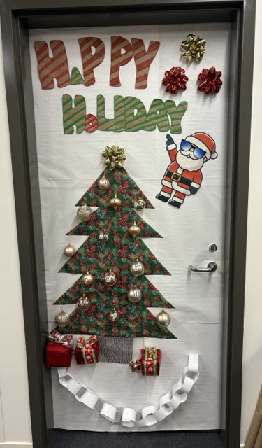 Festively decorated office door with a Christmas tree, Santa Claus illustration, and presents, celebrating the holiday season.
