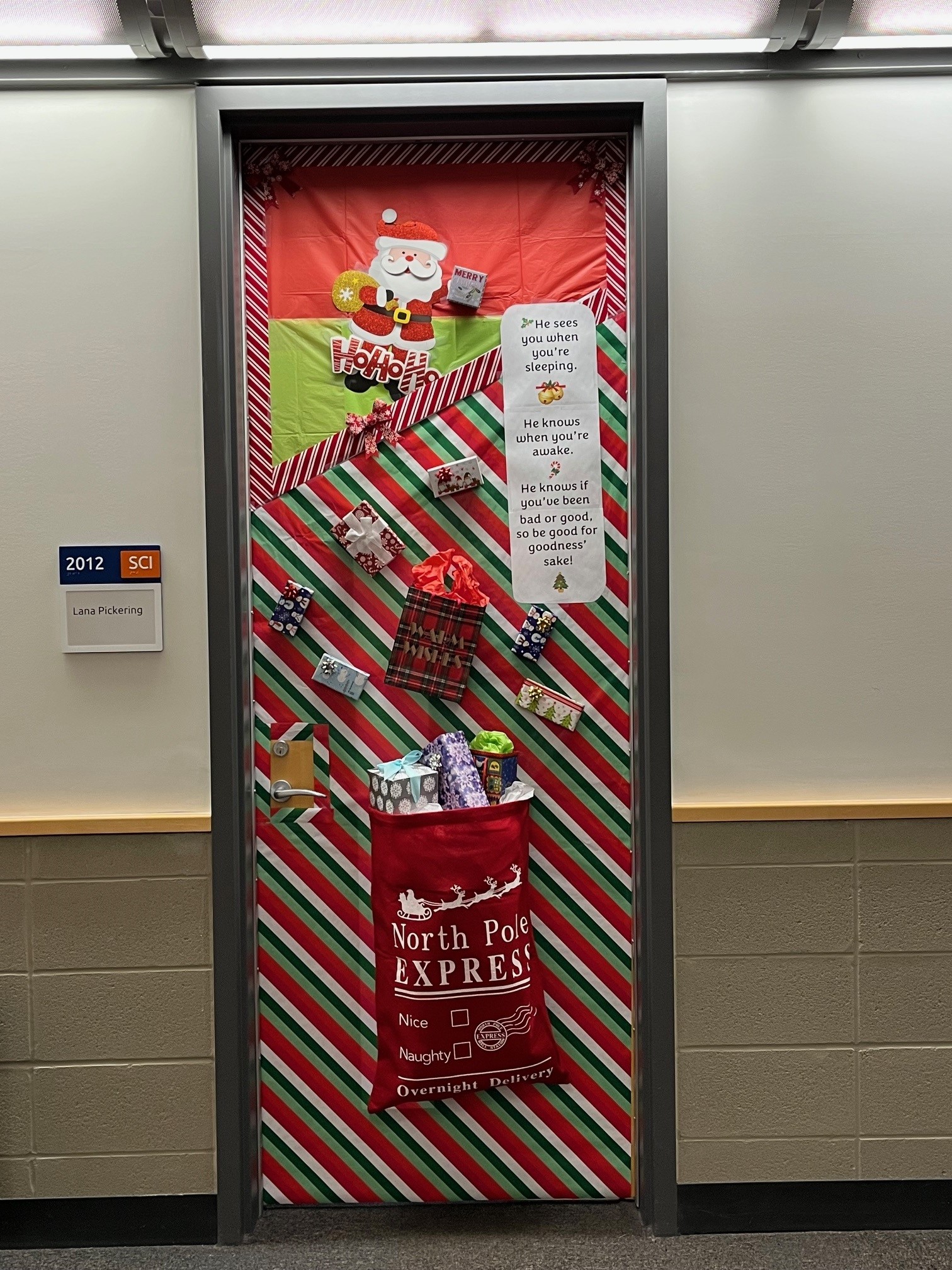 A festive holiday-themed door decoration featuring Santa Claus, Christmas presents, and a "North Pole Express" mailbag.