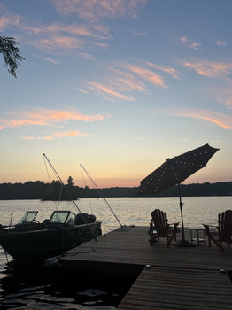 Wooden dock with a boat, Adirondack chairs, and a lakeside sunset at a family cottage.