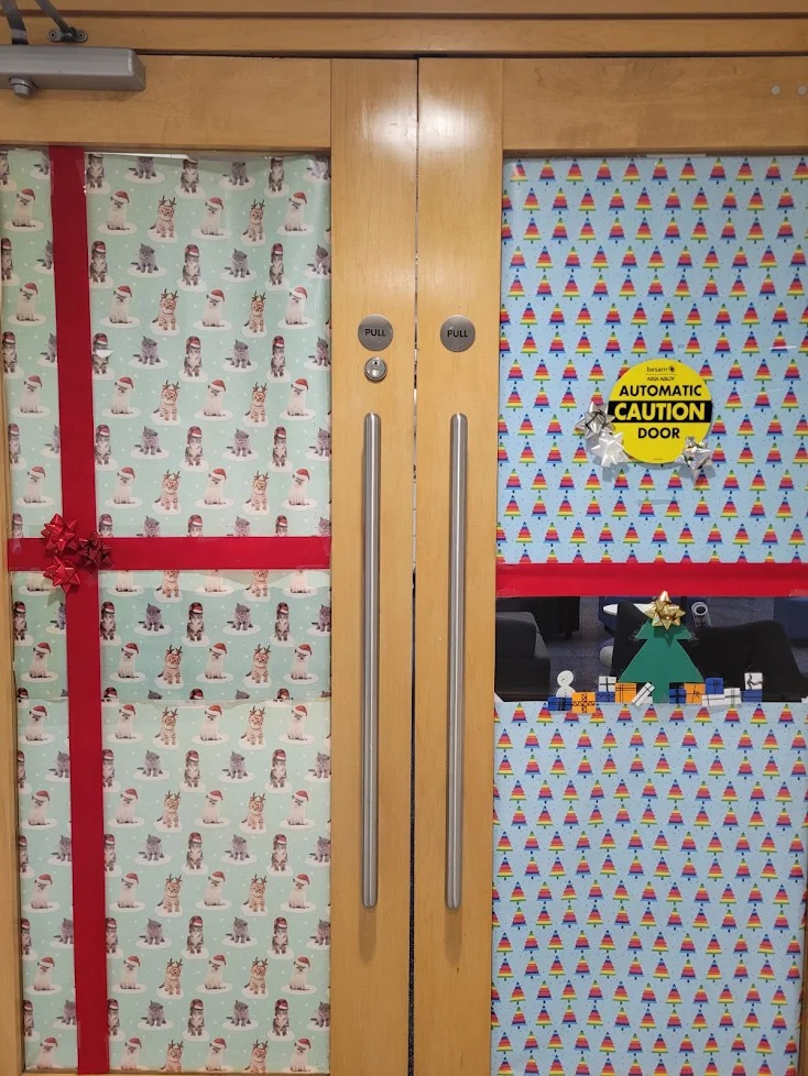 Holiday-themed decorated door featuring festive wrapping paper, a caution sign, and a small festive display.