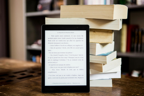 An image of an e reader sitting against a pile of stacked books.