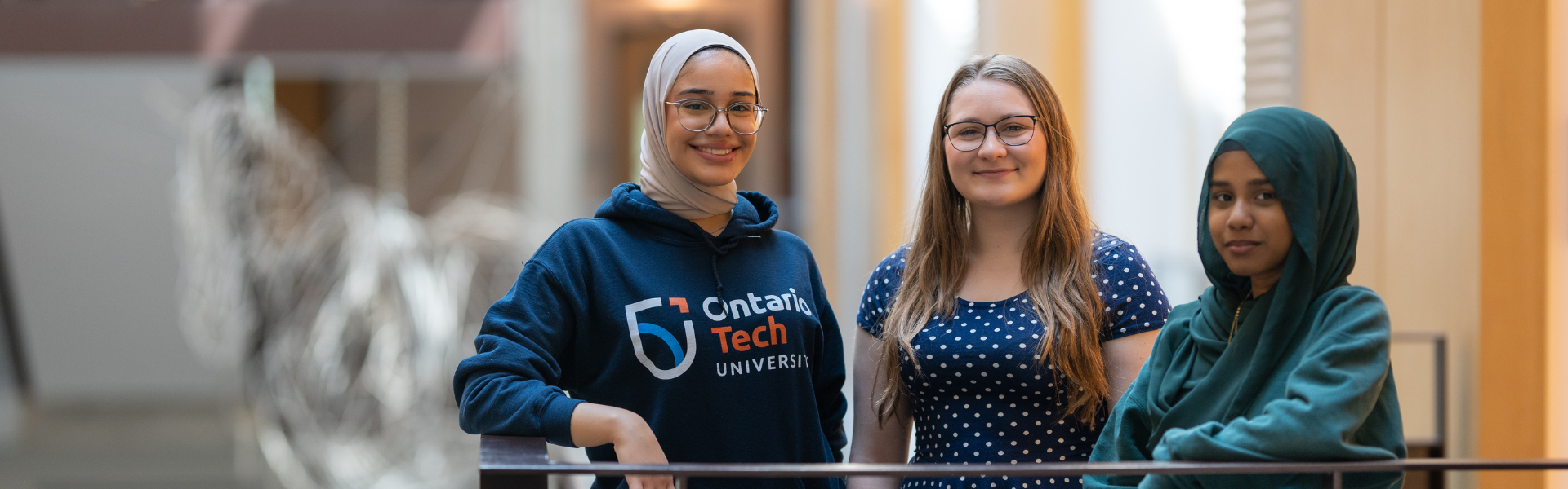 Three female students standing at railing inside a building.