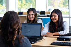 three students at a desk with a laptop