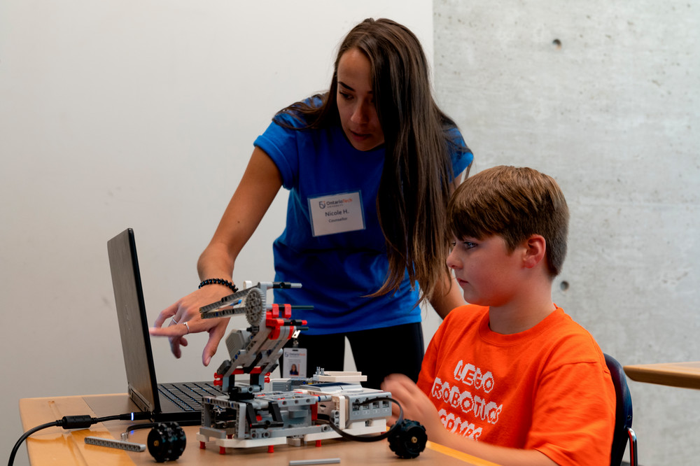 student pointing to a computer, while a younger elementary school student watches