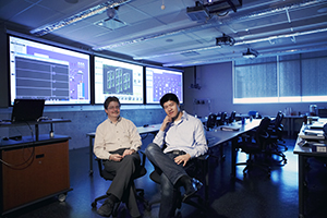 Two seated males pose for a photo inside a lecture room