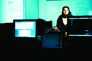 A standing female poses for a photo amongst computers in a classroom