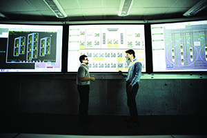 Two students in discussion in front of three large screens full of data