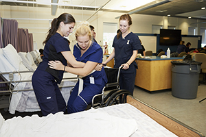 Nursing students helping a patient into a bed.