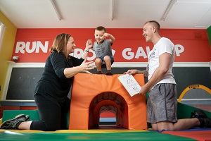 Two students engage with a child who is playing on a mat structure