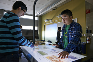 Two male students work on table screen in a classroom