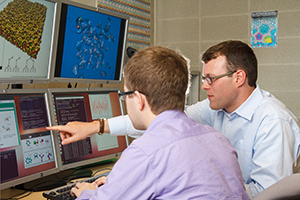 A male instructor points out data on a computer screen to a male student