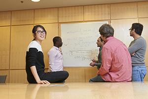 A group of students gather and consult in front of data written on a whiteboard 