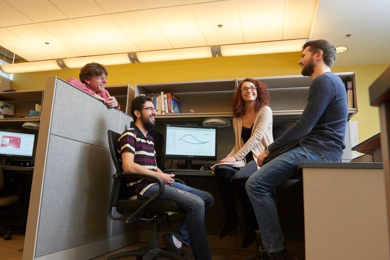 A group of students chat around an office cubicle
