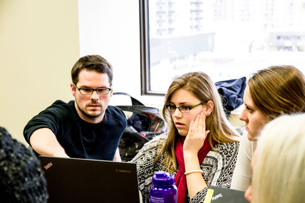 An instructor points something out on a laptop to a group of students