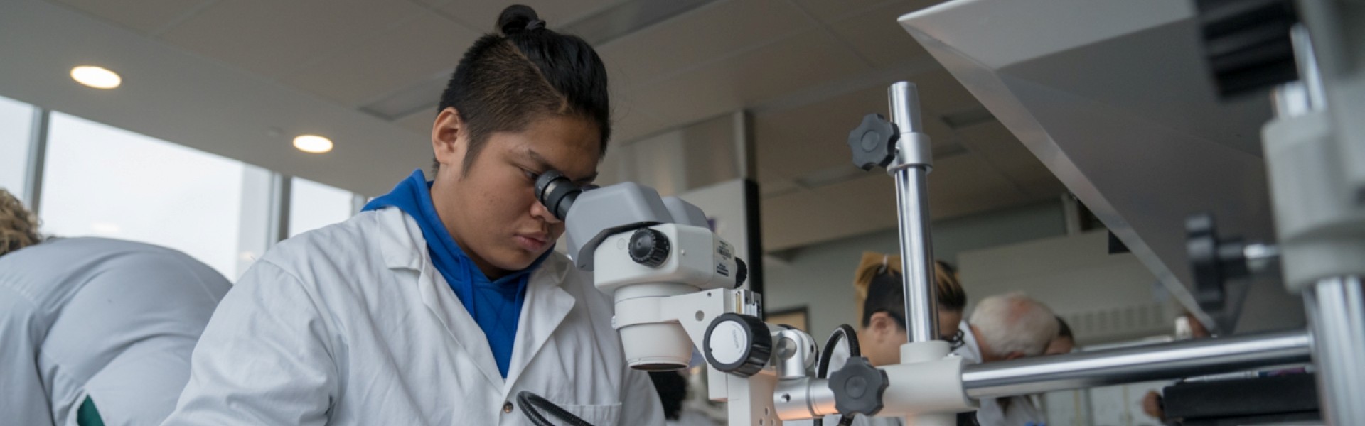 Students/Researchers conducting lab work in white lab coats, which involves using a microscope