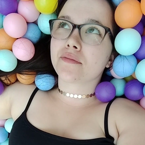 Angelique Dack, a brunette, fare-skinned woman with glasses laying in a pastel ball pit.