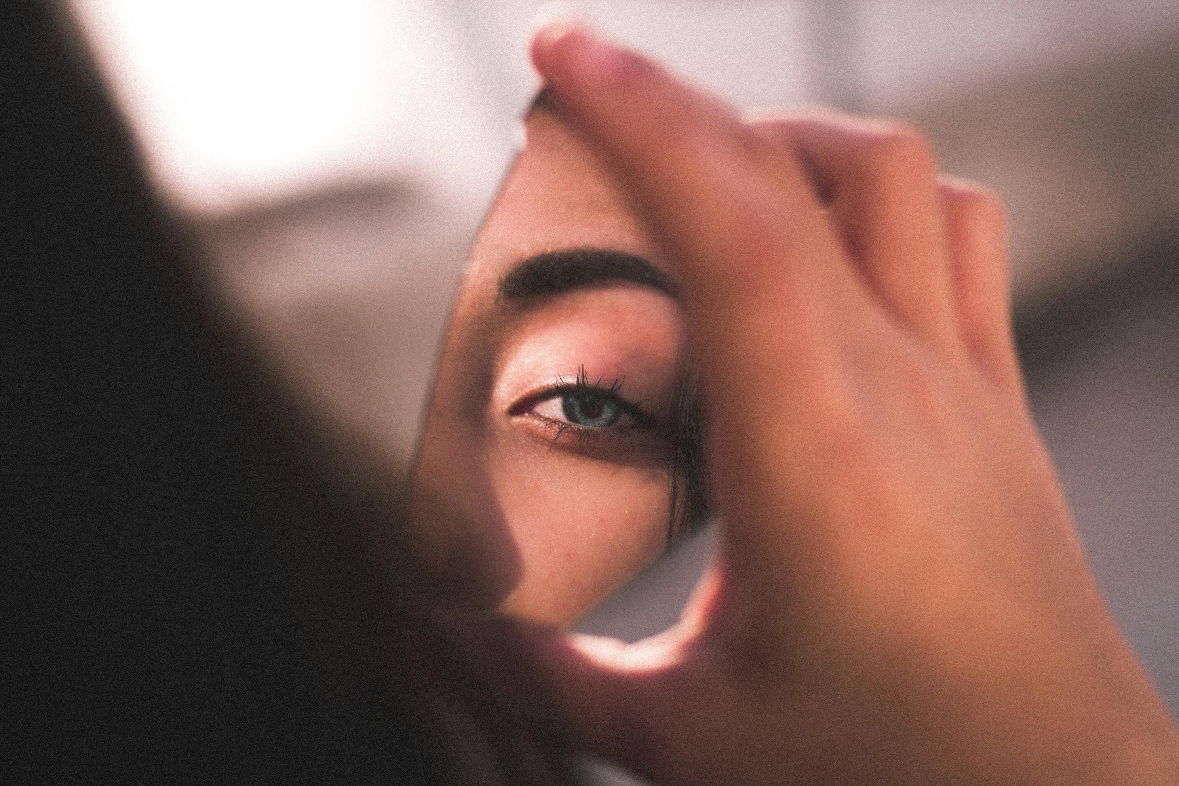 A person holdsa  broken glass mirror with their eye in the reflection