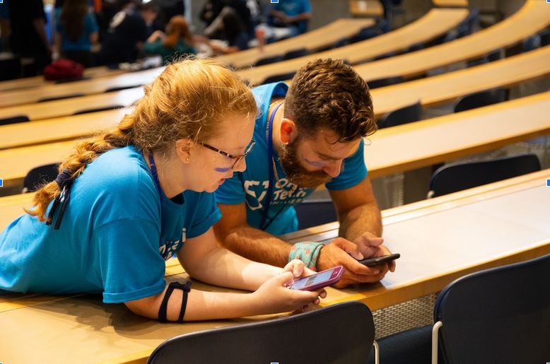 Two students leaning on the desks browsing their phones
