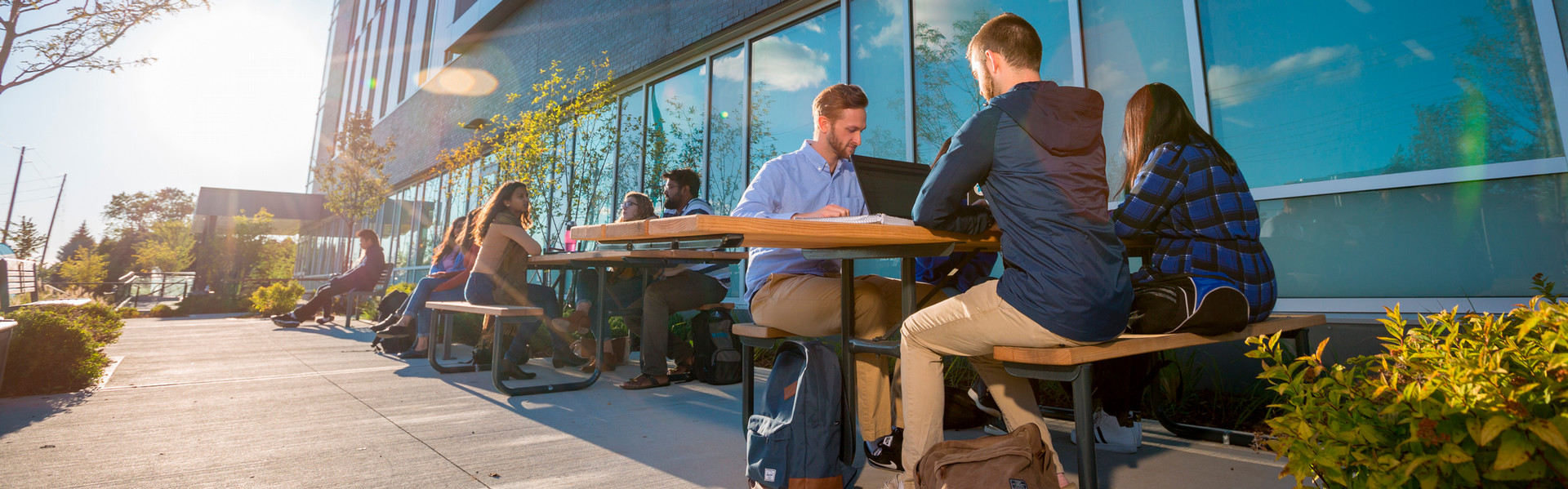 Students studying in groups at tables outside of a campus building.