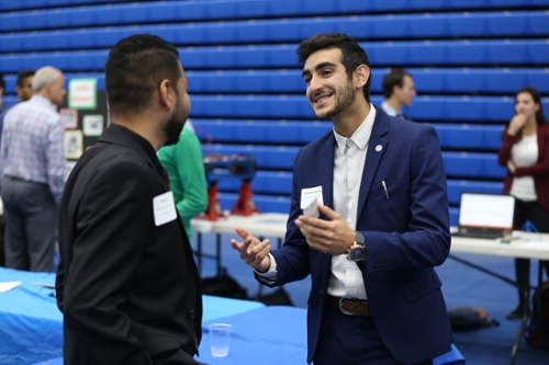 Student in navy suit talking to a student in a black suit at the Engineering Reverse Career Fair